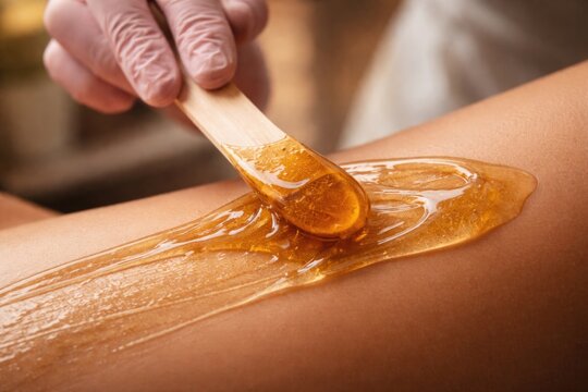 Macro shot of expert sugaring technique for hair removal using honey based wax and spatula indoors