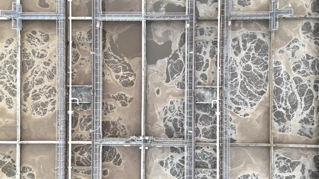 Aerial view of municipal wastewater treatment plant showing sequential stages of sedimentation and filtration processes with visible tanks and infrastructure in a green landscape