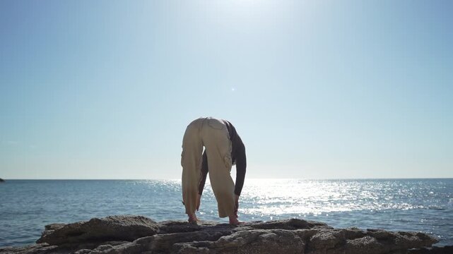 Yoga stretching ocean young woman practicing mindfulness on coastal rocks by the sea under a bright sun for health and serenity