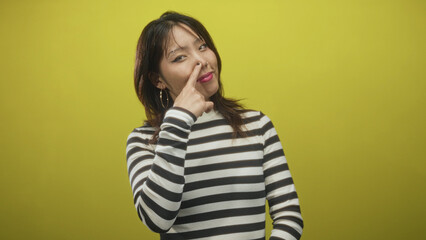 Woman points finger to nose in striped sweater with hoop earring against yellow studio backdrop, closeup pose  playful mischief. © Krakenimages.com