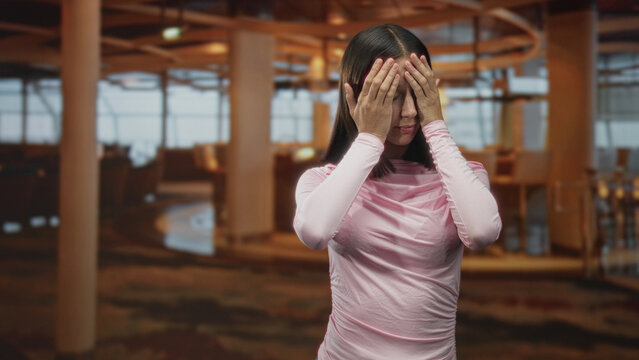 Woman touching forehead with hand and closed eyes in airport terminal wearing pink off shoulder top and visible shoulder; fatigue delay.