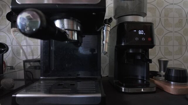 Professional barista's hands inserting a portafilter and placing a glass cup to pour hot water from the coffee machine group head, an essential step for preheating before brewing espresso