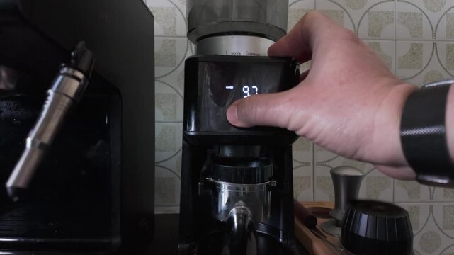 Professional barista adjusting the timer setting on a modern electric burr grinder before milling fresh roasted coffee beans for a perfect espresso shot in a cozy kitchen or specialized cafe
