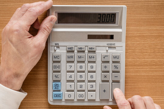 Male hands inputting numbers on calculator, finger pressing keypad, closeup capture of decisive moment, office tabletop suggesting transaction and cashflow planning