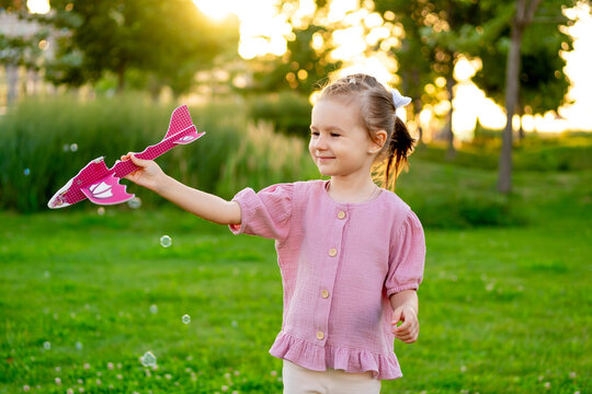 a child launches a plane in the summer on a green lawn, a happy childhood, a little girl having fun outside, laughing and playing with a plane