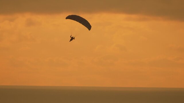 Paraglider sunset flight silhouetted paraglider glides through a golden sky over the ocean during a peaceful evening at dusk