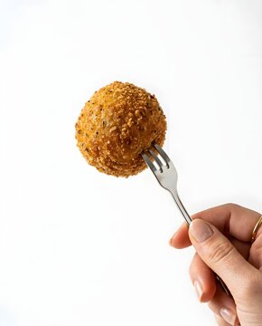 Close up of golden fried food item impaled on a fork against white backdrop