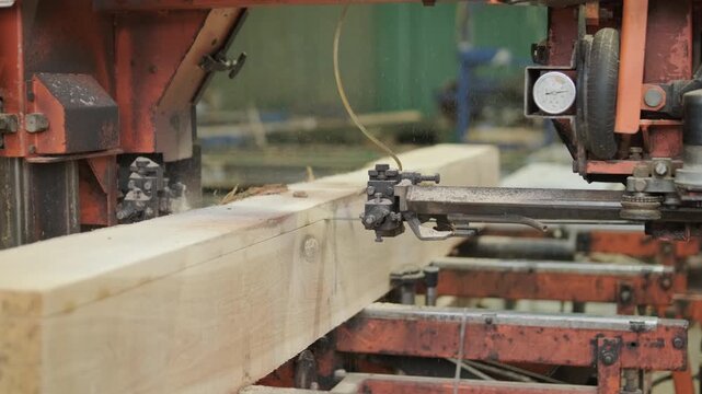A heavy-duty sawmill machine trimming a large log to create a rectangular beam, controlled by a professional operator