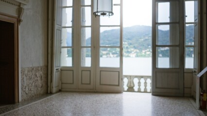 Obraz premium Interior room with open french doors leading to a lakeside balcony, soft defocused bokeh view of water and distant hills; background backdrop copyspace calm.