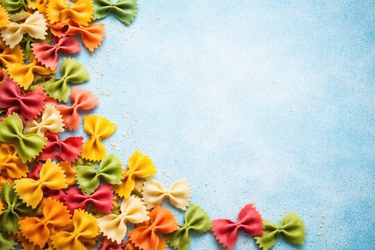 Multicolored bowtie pasta arranged on a high key blue grainy texture with copy space