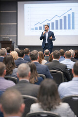Obraz premium Man speaks to audience during business presentation. He gestures toward upward-trending graph on screen. Attendees sit attentively in rows of chairs