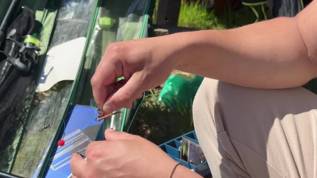 Fisherman placing a worm on a fishing hook during outdoor fishing, close-up action scene