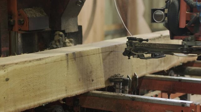 A heavy-duty sawmill machine trimming a large log to create a rectangular beam, controlled by a professional operator