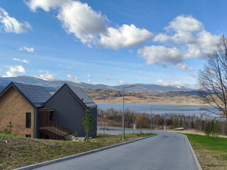 Obraz premium Road leading toward lake and modern holiday houses under dramatic sky. Concept of travel destination, freedom, scenic landscape, peaceful vacation.