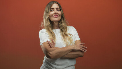 Obraz premium Woman smiling and posing, gesturing with a blurred hand and later folding crossed arms while wearing a white t shirt against an orange studio backdrop; confidence warmth.