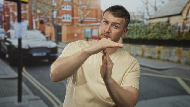 Man making timeout gesture with hands on a city street in front of brick building and parked car; frustration warning.