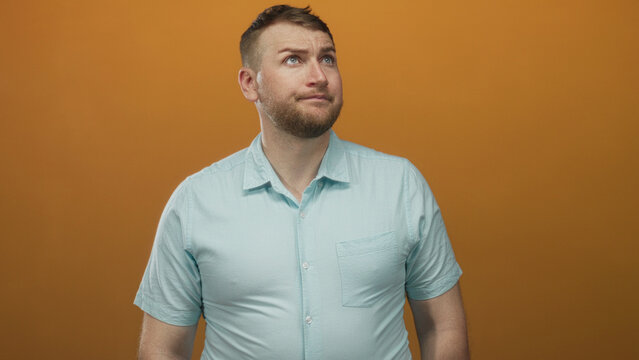 Man with raised eyebrow and puzzled gaze wearing light blue shirt and short sleeves in orange studio setting; uncertainty reflection.