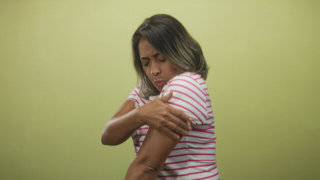 Woman middle aged hispanic rubbing her forearm and wincing while holding elbow, wearing striped shirt in studio; pain.