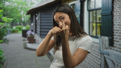 Fototapeta premium Woman with fists raised in a boxing pose beside a building exterior, smiling and showing knuckles in a casual white tshirt; playful training.