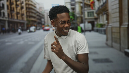 Naklejka premium Man in white polo shirt dancing with raised finger on street lined with shops and traffic; joy celebration fun liberation.