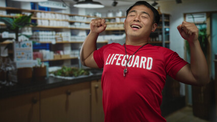 Young chinese lifeguard man wearing red shirt and whistle stands with folded hands in a pharmacy building  serenity. © Krakenimages.com