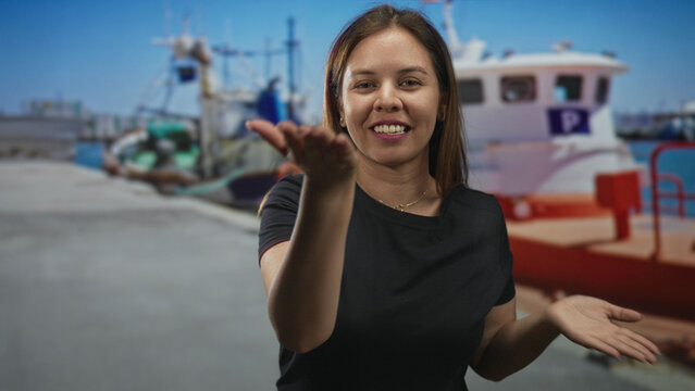 Young woman blowing a kiss with hand at a sunlit port pier by boats and seaside; affection greeting.