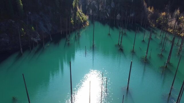 High angle view of mystical turquoise lake with submerged trees and bright sun reflection, Tian Shan mountains, Kazakhstan, Kaindy Lake. High quality 4k footage