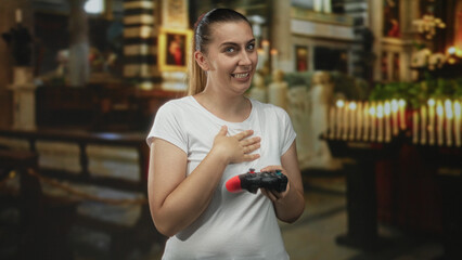 Woman laughing while holding a gamepad and placing hand on chest in a church building with lit candles and pews visible  playful amusement. © Krakenimages.com