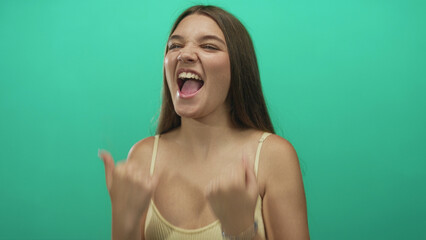 Naklejka premium Teenage girl clenches fists while smiling broadly in mint green studio setting showcasing victory gesture; excitement triumph celebration.