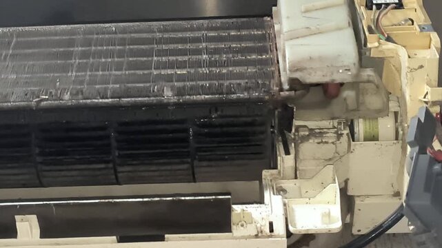 Technician washing reusable split AC air filter under water during appliance maintenance procedure. Cleaning process improving indoor air quality and efficient cooling performance in modern AC