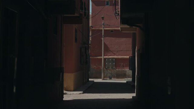 View through dark doorway into sunlit narrow street with terracotta walls utility pole and cables in Moroccan town