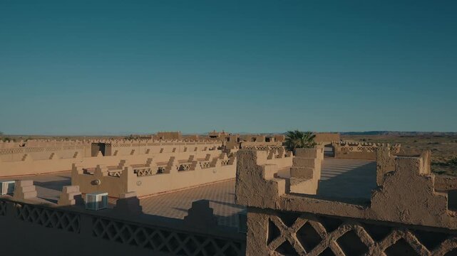 View from rooftop over flat clay rooftops decorative mud brick walls and desert town stretching to horizon under clear blue sky