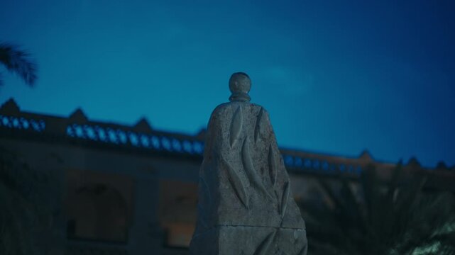 Rock stone monument or sculpture standing outside lit kasbah wall under deep blue night sky in Morocco