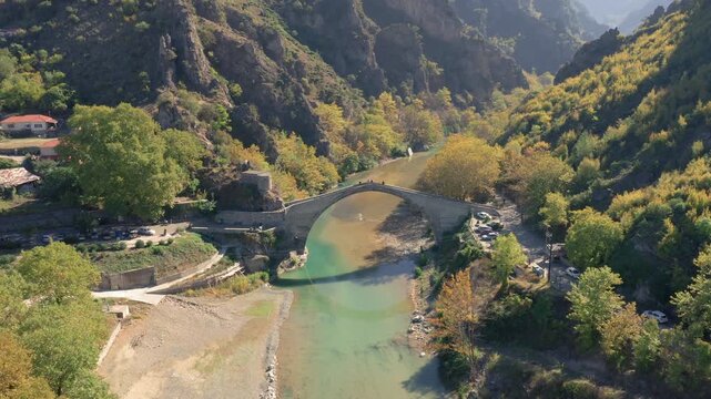 Slow panning drone shot of Konitsa stone bridge spanning Aoos river in Epirus, Greece under bright spring sunshine