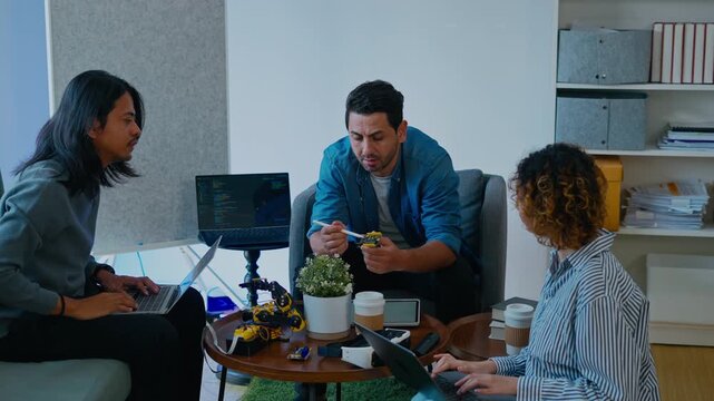 Group of young engineers meeting and explaining robot hardware and software program.Professional team collaborating on robotics technology and innovative electronics project in modern startup office