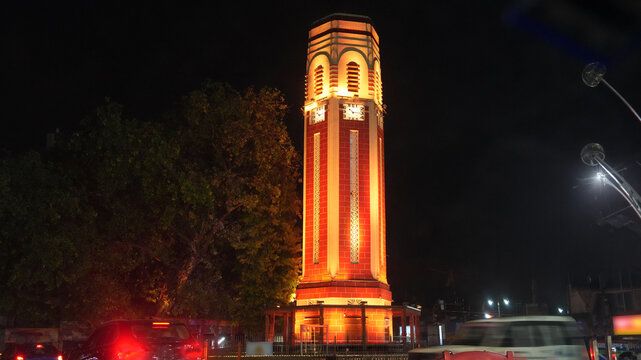 Night view of the illuminated Dehradun Clock Tower in Uttarakhand, India, glowing with warm architectural lighting against a dark sky. A landmark city scene featuring historic tower architecture