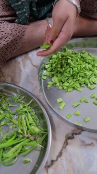 close-up of a person's hands cutting fresh green cluster beans (Gwar Phali) on a steel plate