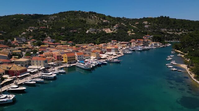 Drone footage of Mediterranean harbor in Greece, Paxos island, Gaios marina in summer, turquoise water with boats, red-roofed hillside houses and scenic coastal landscape