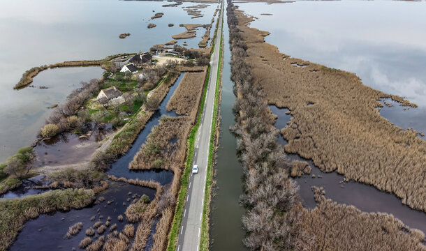 Aerial view of the Scamandre Regional Nature Reserve with a straight road crossing wetlands and traditional houses in Arles, Provence-Alpes-Cote d'Azur, France.