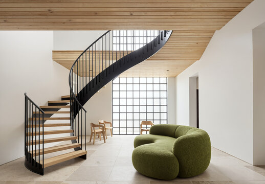 Modern spiral staircase with green sofa in minimalist white interior space.