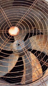 The video shows a close-up view of a large, rusty industrial fan in operation. The fan is covered by a circular wire grille that is heavily corroded with orange and brown rust.