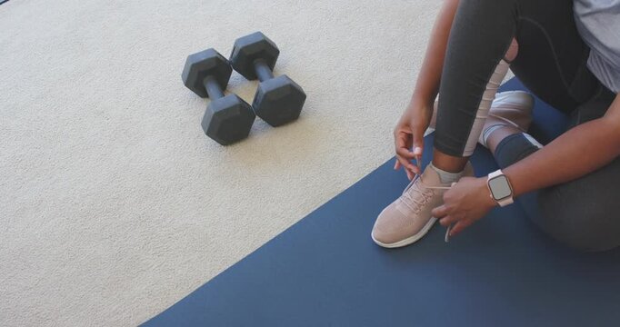African American woman in tights seeing weights reaching, tying laces at home prepping, copy space