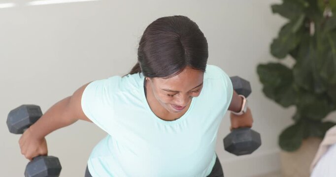 African woman gripping weights, lifting rear flies, smiling, keeping form at home for strength