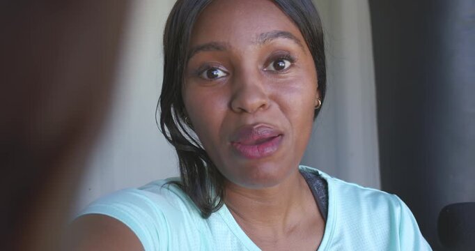 African American woman leaning in, filming, gesturing, earbud, finger at left, smiling, waving