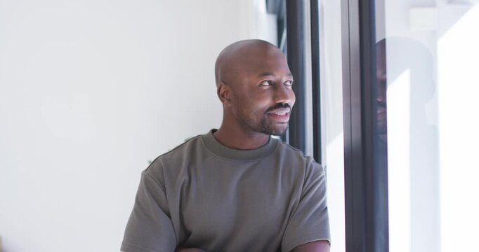 African adult male standing by window in room, noticing reflection, turning to camera and smiling
