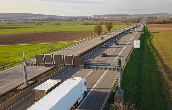 Aerial view of trucks and cars on the autobahn with the digital speed limit signs, traveling between agricultural fields 