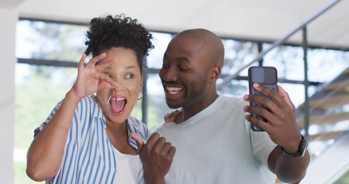African American couple receiving live call, holding smartphone, sharing red key fob near grid pane