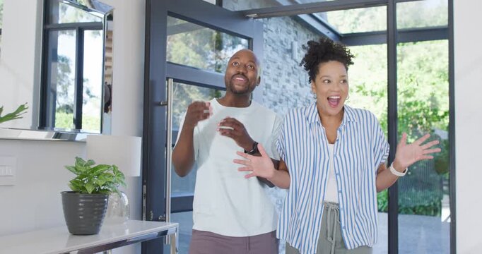 African American couple opening glass pivot door, entering home and hugging, celebrating arrival