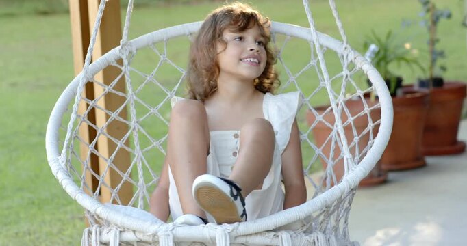 African American child girl age 6 shifting in woven hanging chair on porch, following sunlight
