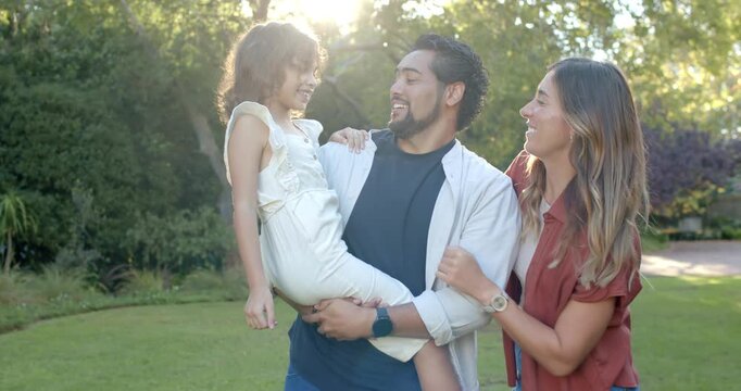 Diverse family standing on lawn man holding daughter in light dress woman tickling making her laugh